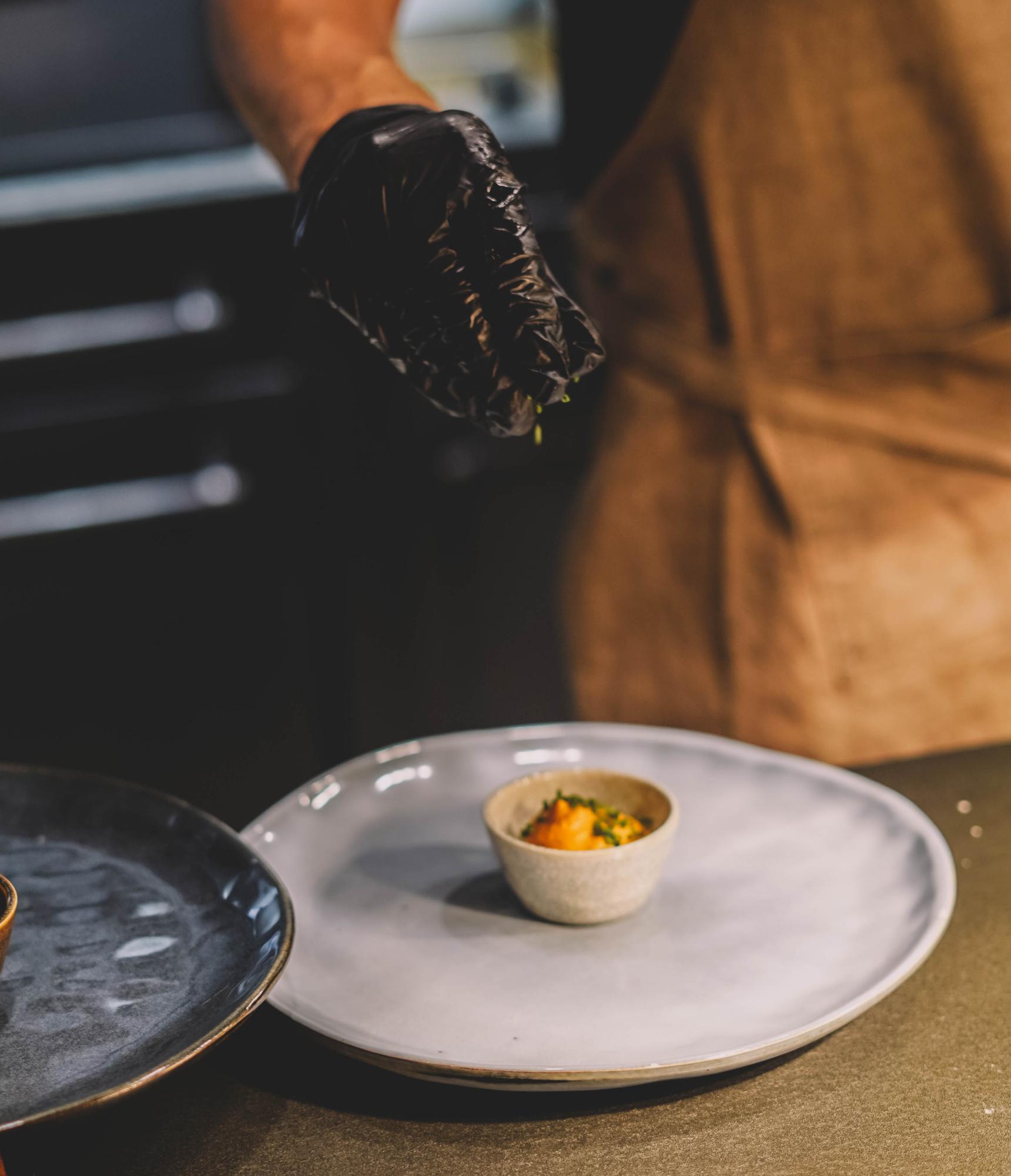 Chef plating a composed dish on dark table
